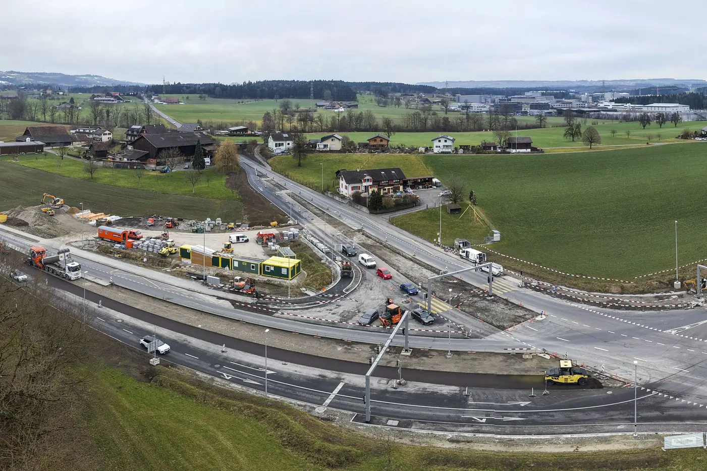 Baustelle an einer Verkehrsader mit grünen Wiesen und Wohnhäusern im Hintergrund.
