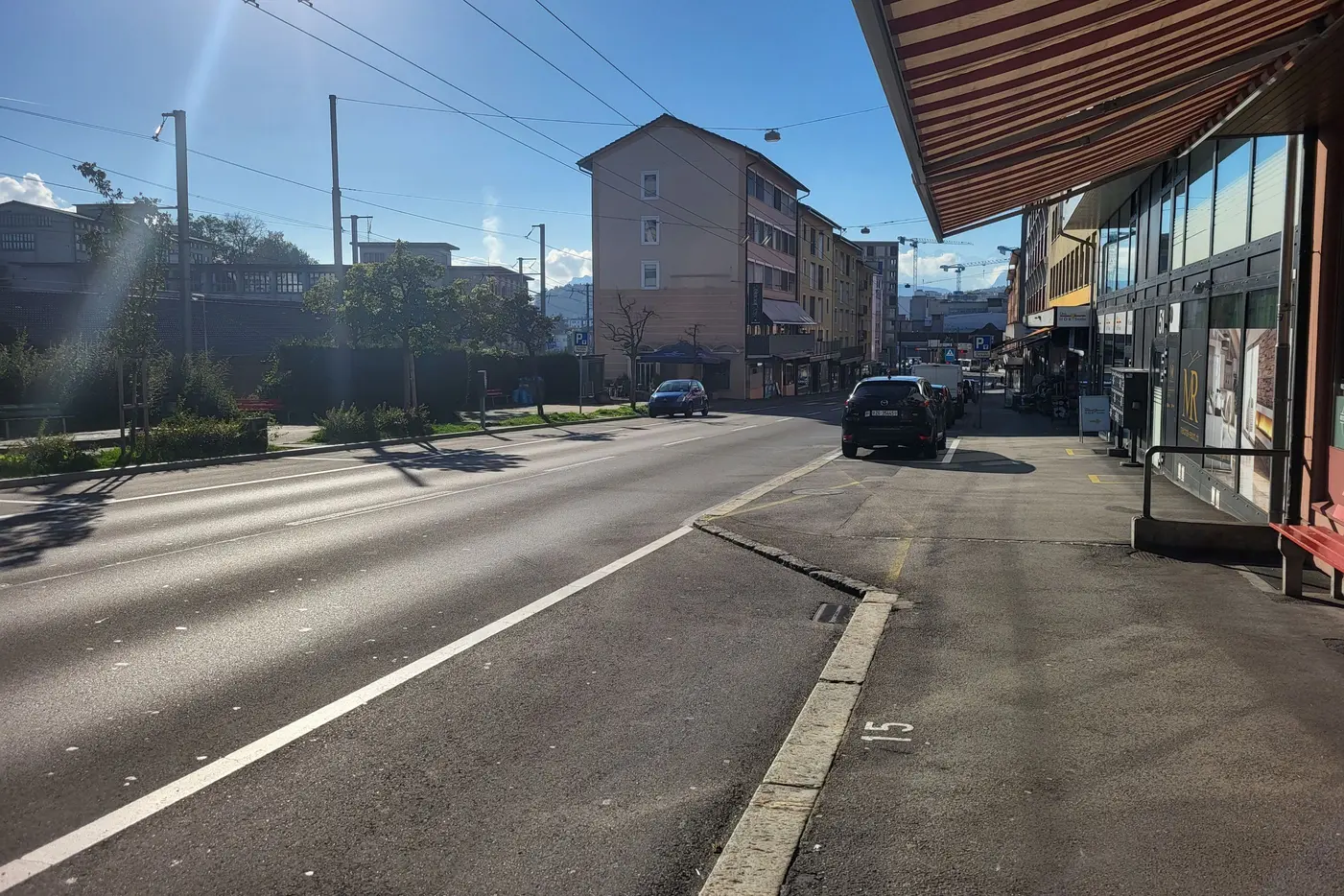 Blick auf eine Straße mit sonnigem Himmel, Wohngebäuden und geparktem Auto.