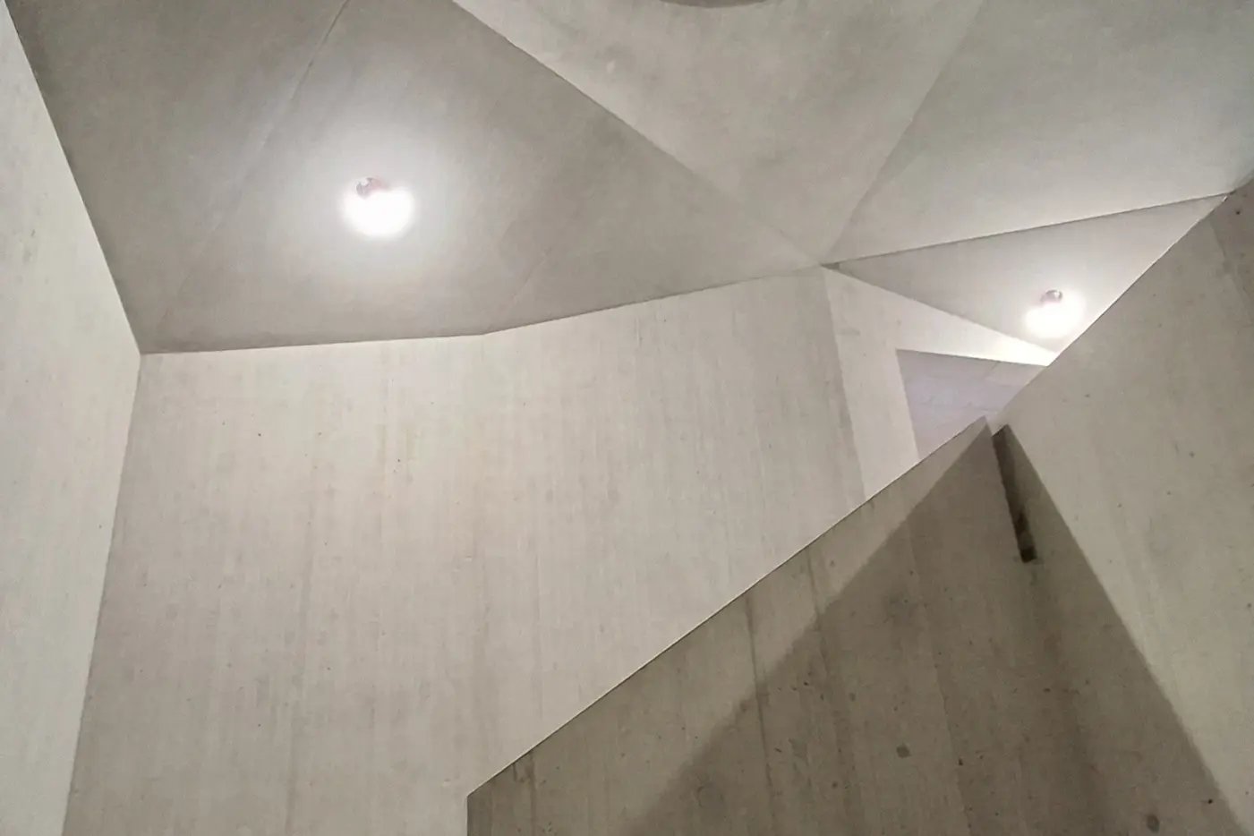 Betonwände mit geometrischen Formen und einem runden Lichtausschnitt oben.