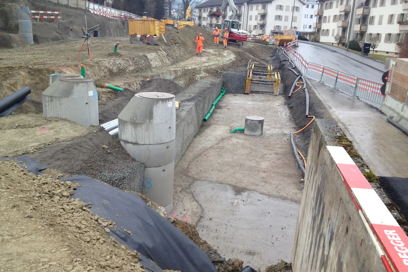 Baustelle mit Graben für Fundament, umgeben von Maschinen und Baufahrern.