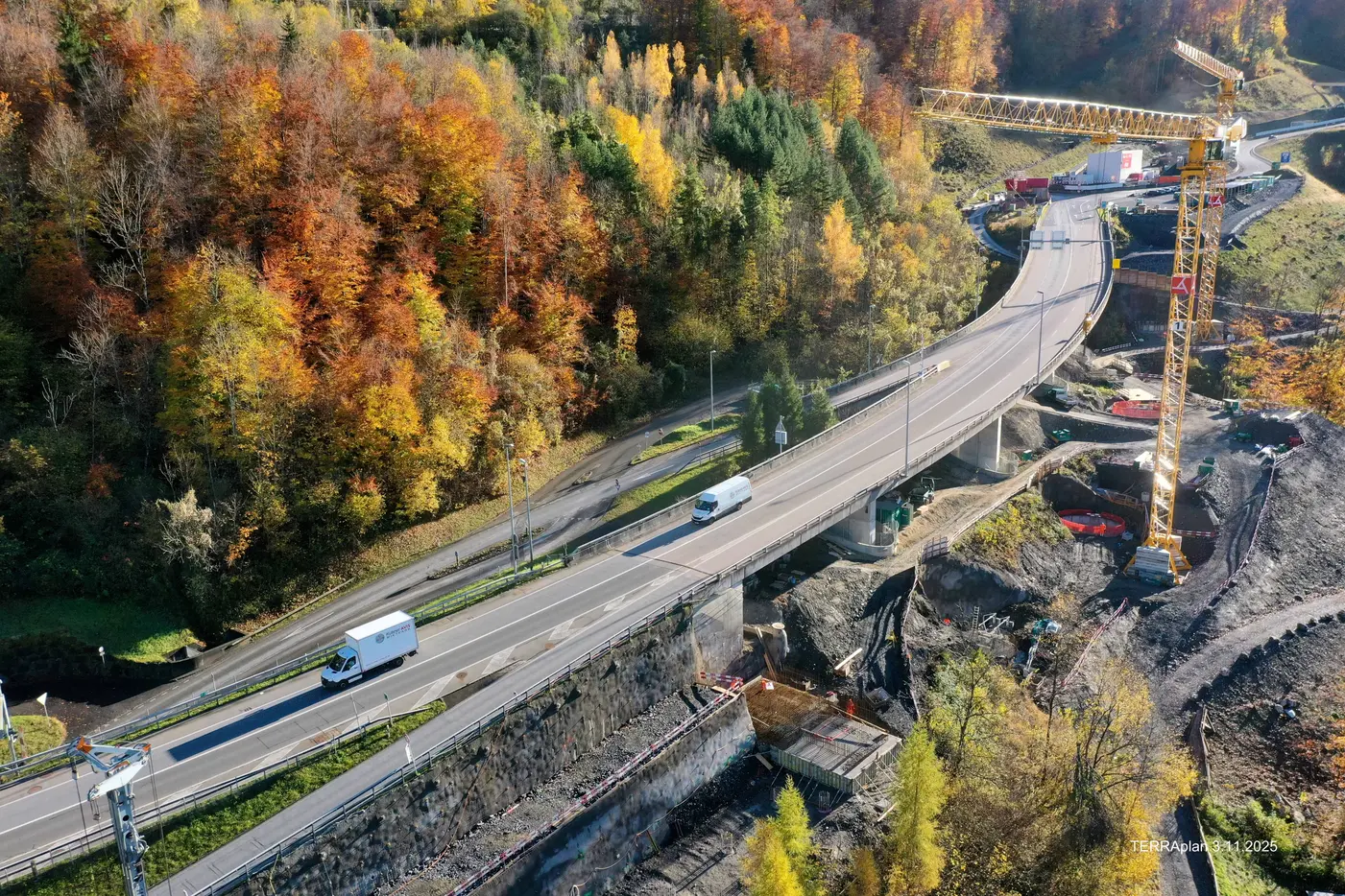 Blick auf eine kurvenreiche Straße in herbstlicher Landschaft mit Baustelleninfrastruktur.