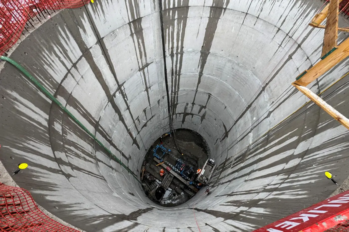 Blick in einen tiefen, betonsanierten Schacht mit Geräten am Boden.