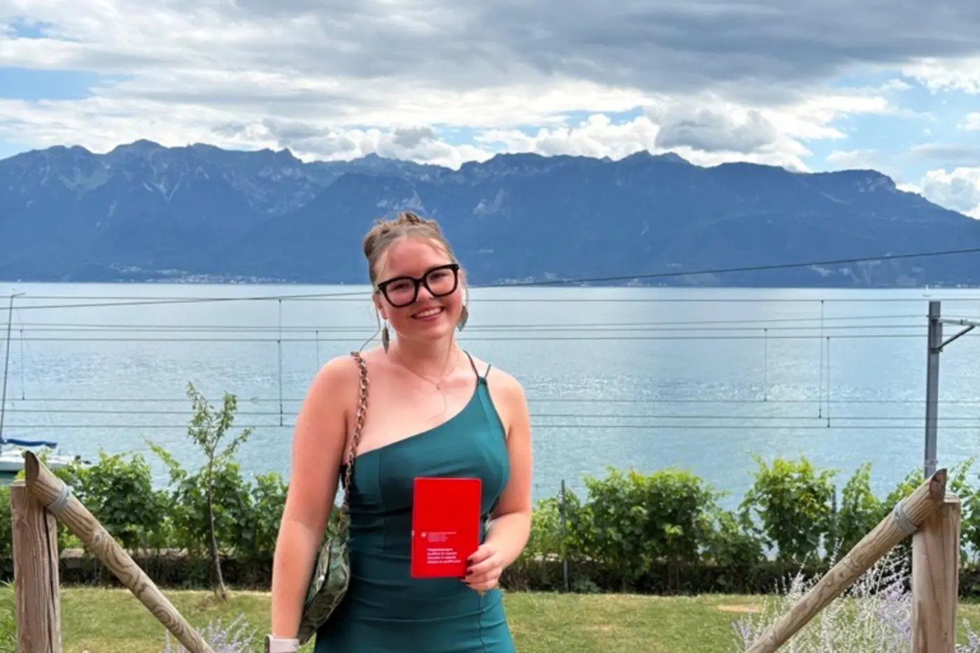 Frau in grünem Kleid steht am See mit Bergen im Hintergrund.