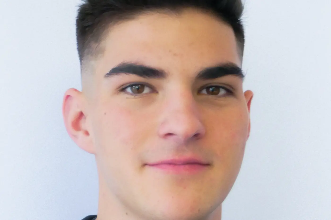 Junger Mann mit kurzem, dunklem Haar vor einem hellen Hintergrund.