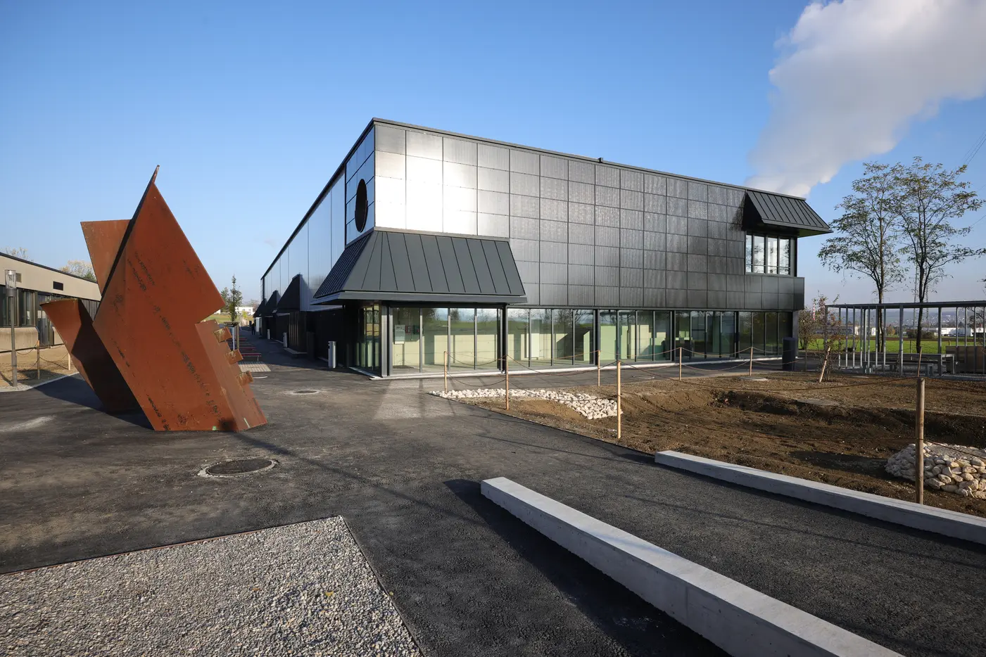 Moderne Gebäude mit Glasfassade, skulpturales Element aus Metall im Vordergrund.