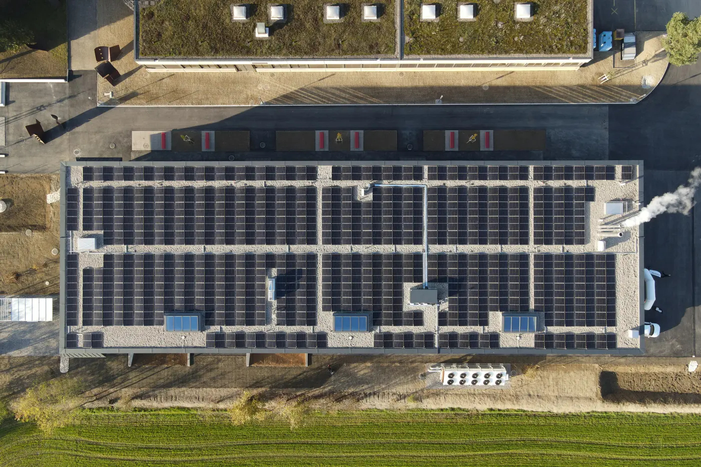 Dach mit Solarpanelen über einem modernen Gebäude, umgeben von Grünflächen.