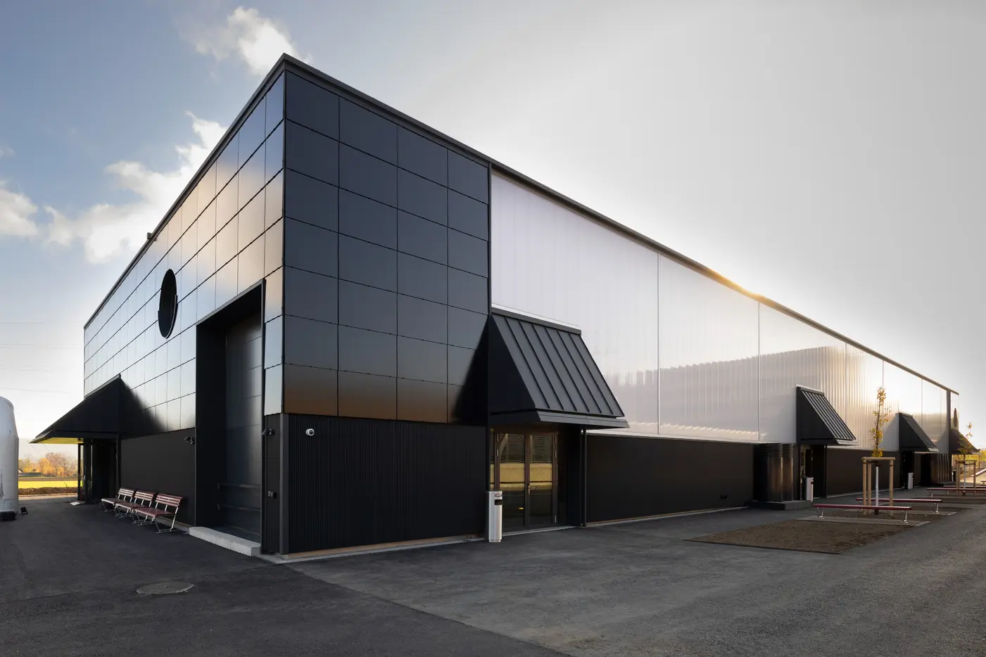 Moderne, schwarze Lagerhalle unter blauem Himmel mit Personen im Vordergrund.