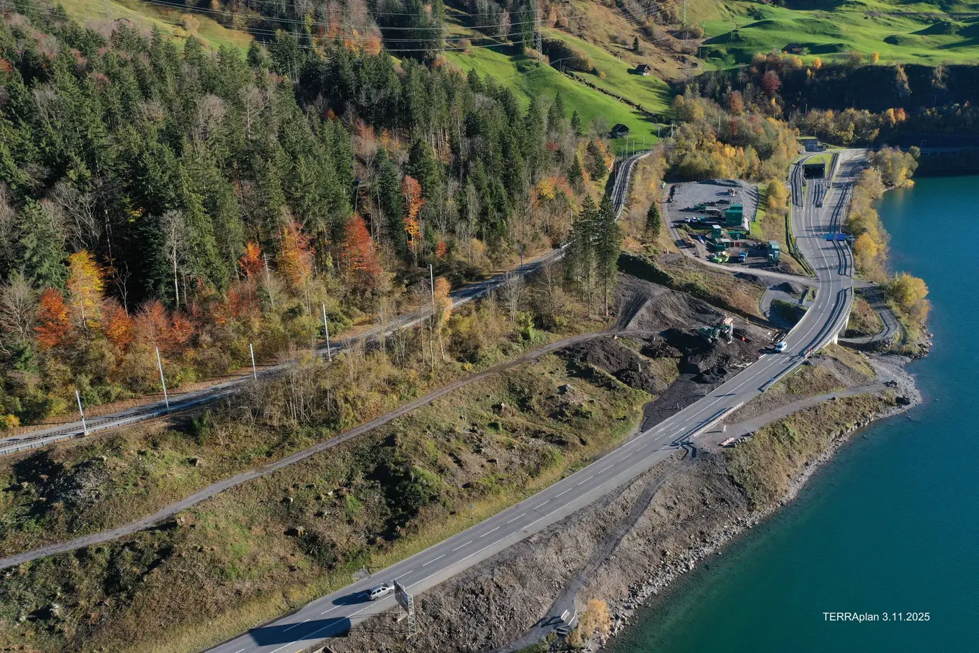 Luftaufnahme einer kurvigen Straße am Ufer eines Sees umgeben von buntem Herbstlaub.