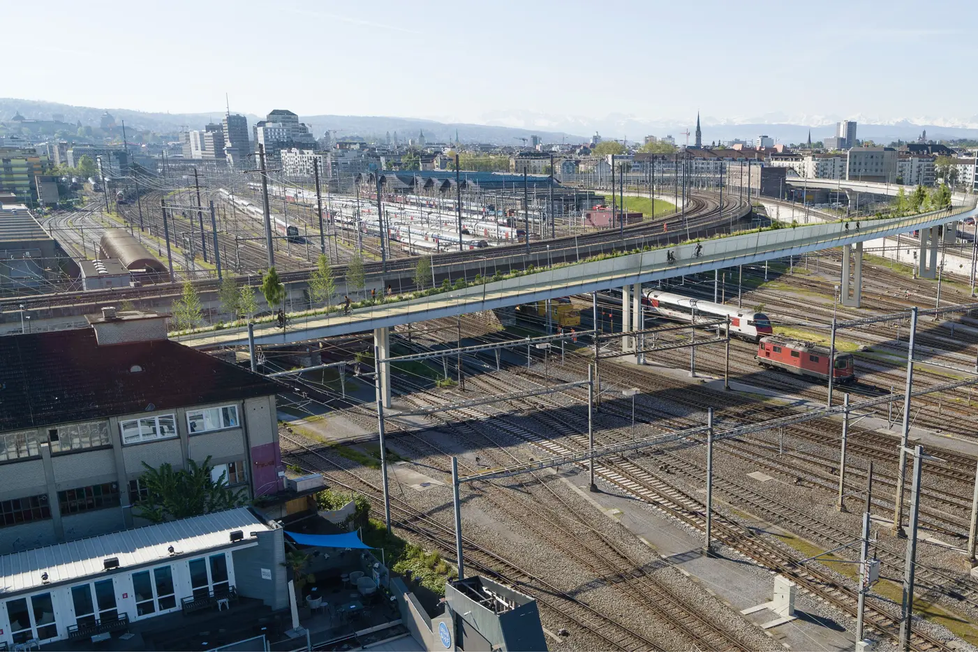 Blick auf ein Bahndepot mit Gleisen und einem Zug unter einem Überweg.