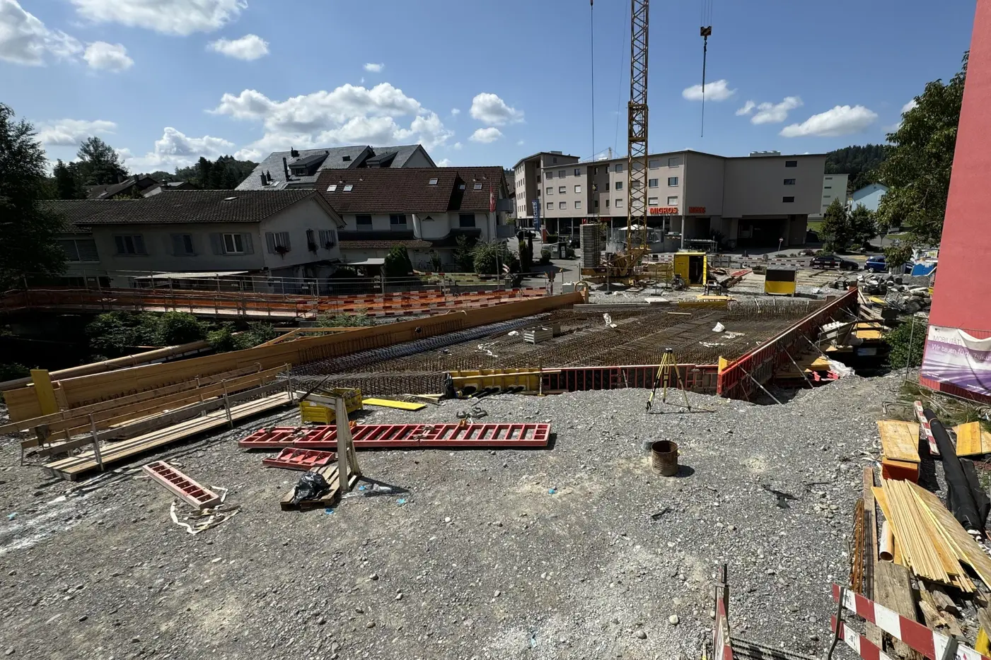 Bauplatz mit Holzgerüst und Baustellenmaterial unter blauem Himmel.