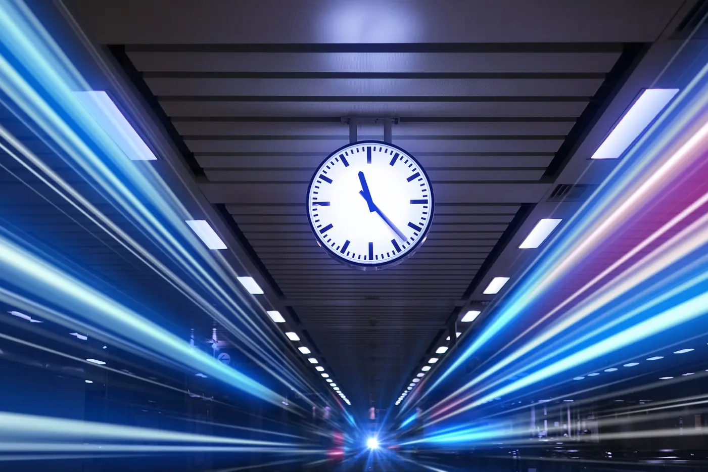 A clock mounted on a ceiling of a train station with vibrant light streaks suggesting movement.
