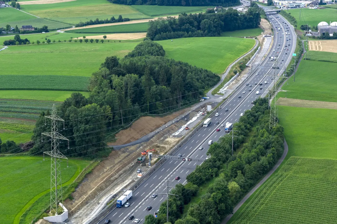 Blick auf eine Autobahn mit Fahrzeugen, umgeben von grünen Feldern und Bäumen.