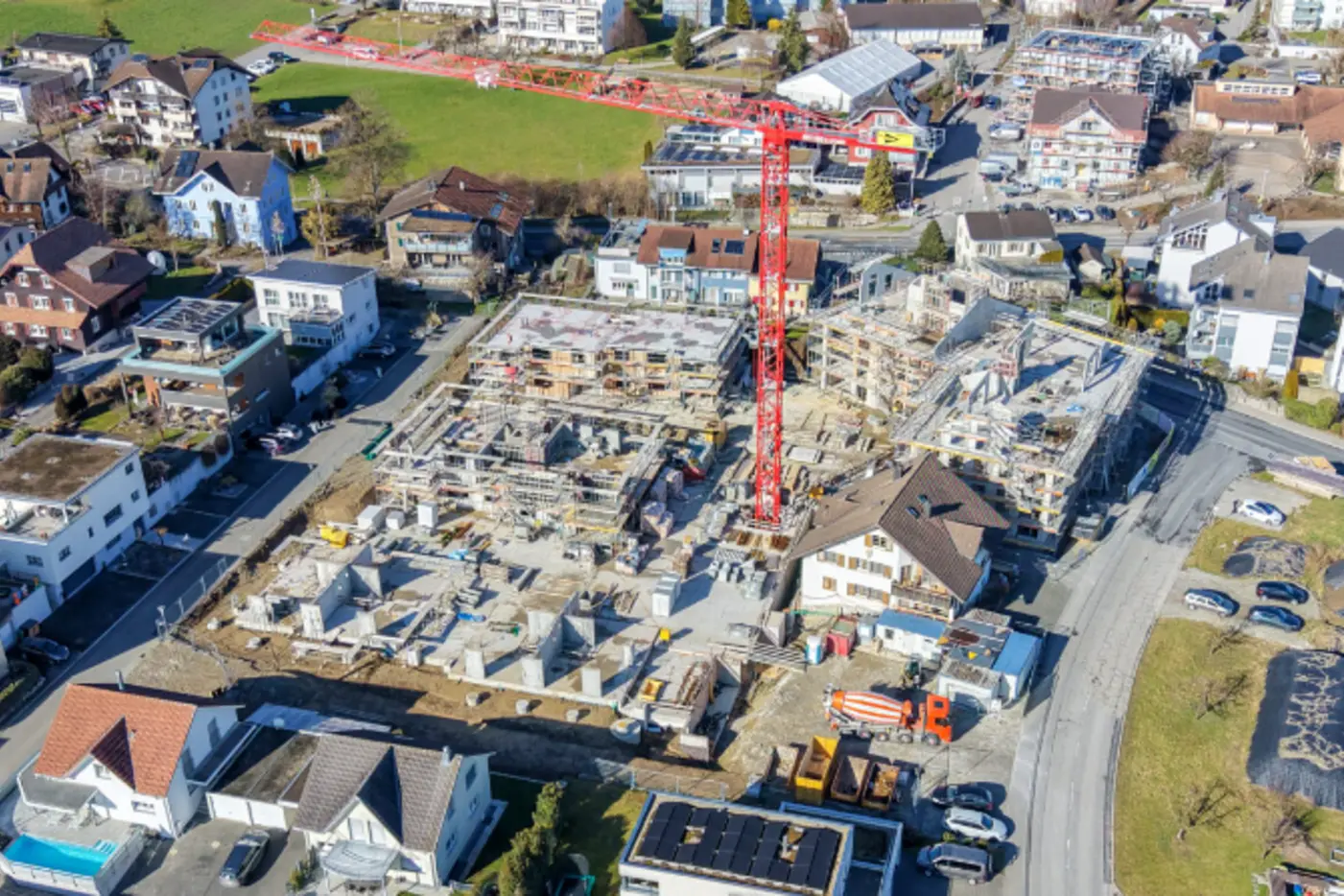 Blick auf eine Baustelle mit einem Kran, umgeben von Wohnhäusern und grünen Flächen.