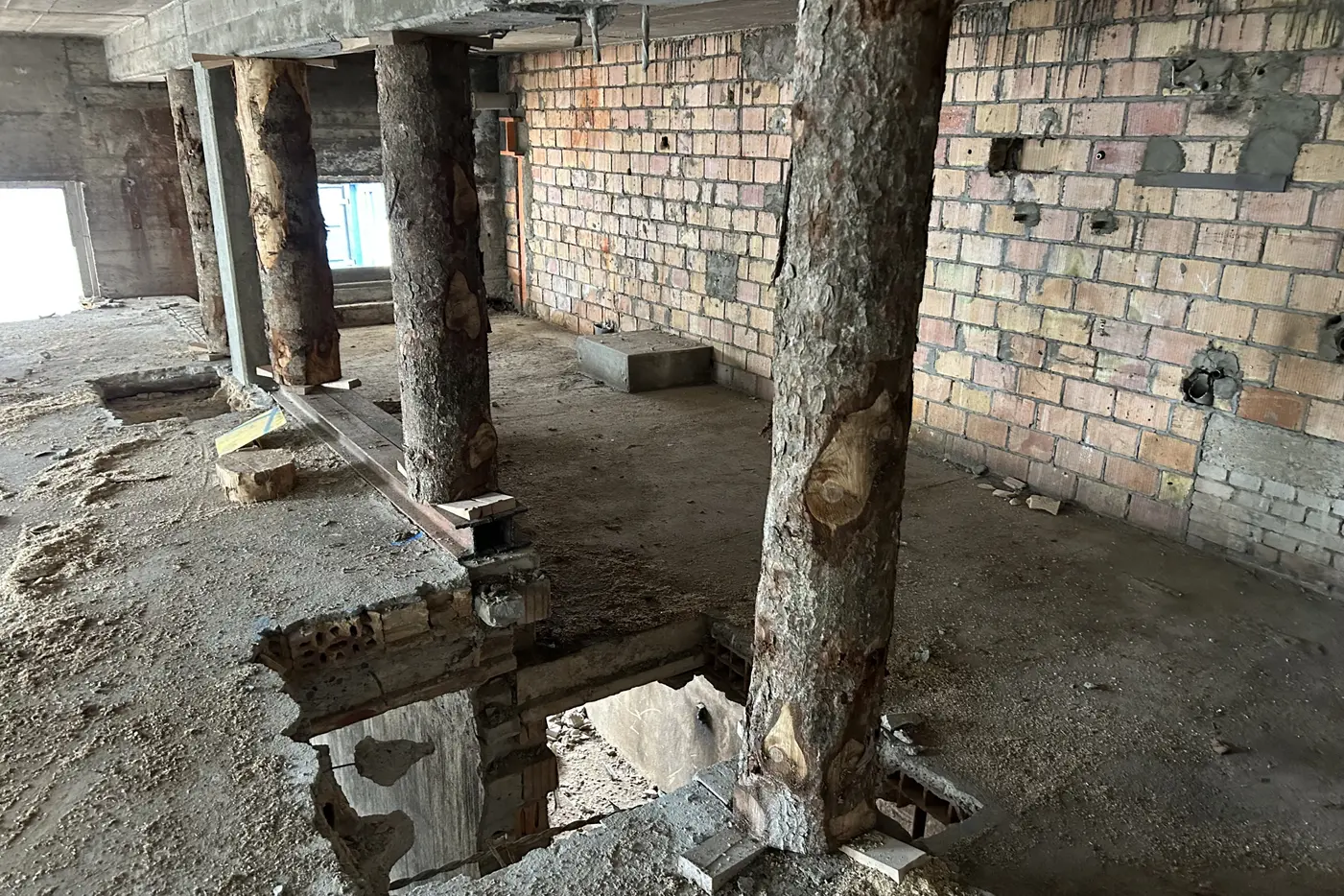 Rohbau mit sichtbaren Holzsäulen, unebenem Boden und Backsteinwänden.