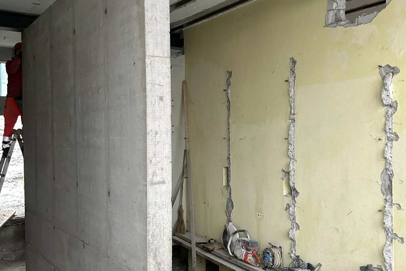 Bauarbeiten mit einer Betonwand, freiliegenden Rohren und Baustellenwerkzeugen.