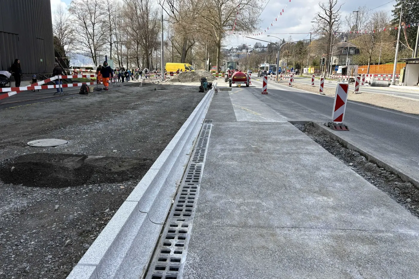 Bauarbeiten an einer Straße mit neuen Bordsteinen und Schotterflächen, Baustellenverkehrssicherung.