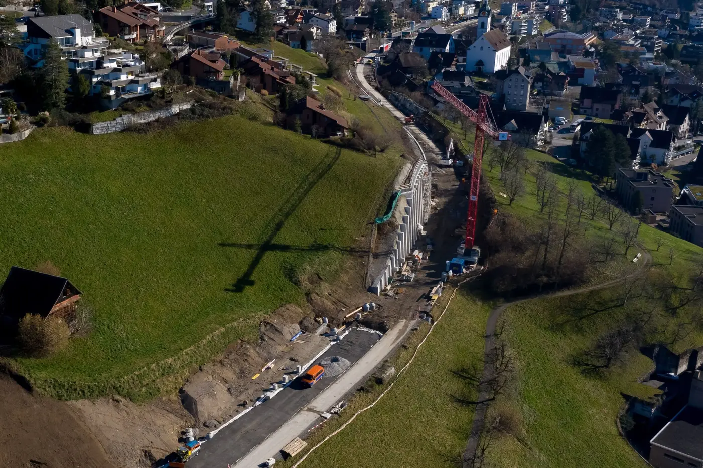 Blick auf eine Baustelle mit Baumaschinen und Hochbau in einer hügeligen Landschaft.