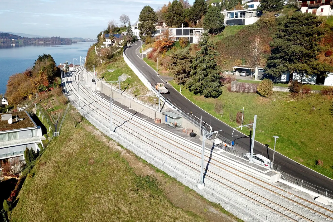 Blick auf eine kurvige Bahnstrecke neben einem Hügel und einem See, umgeben von Wohnhäusern.