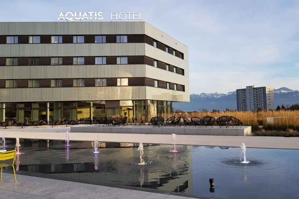 Modernes Hotelgebäude mit Wasserfontänen und Bergsicht im Hintergrund.