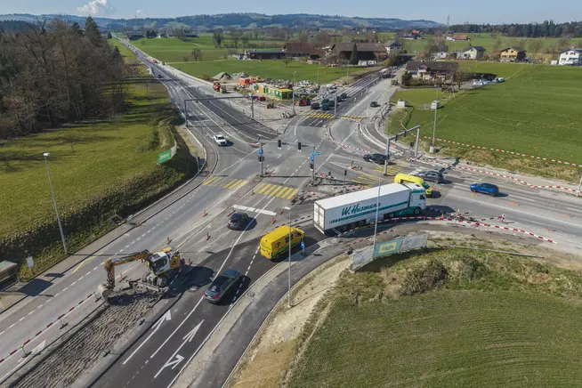 Kreuzung mit Baustelle, mehrere Fahrzeuge und grünen Landschaften im Hintergrund.