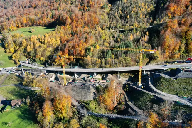 Bau einer Brücke umgeben von buntem Herbstlaub und Kränen.