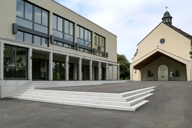 Modernes Gebäude mit Glasfassade und Treppe neben einer traditionellen Kapelle.