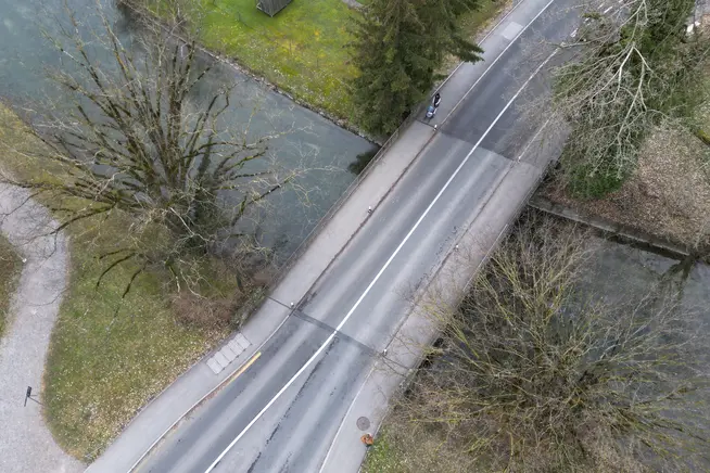 Eine Straße mit Bäumen und einem kleinen Fluss auf beiden Seiten, aus der Vogelperspektive.