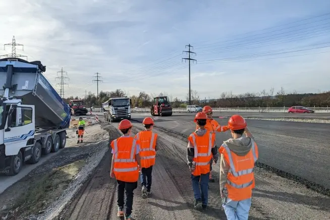 Gruppen von Bauarbeitern in orangefarbenen Westen auf einer Baustelle.