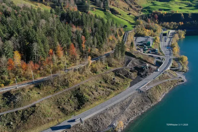 Luftaufnahme einer kurvigen Straße am Ufer eines Sees umgeben von buntem Herbstlaub.