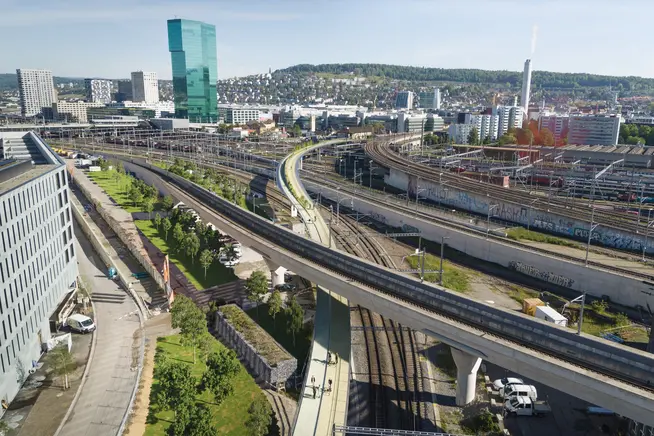 Stadtansicht mit Verkehrswegen, Bahngleisen und modernen Gebäuden im Hintergrund.
