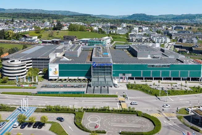Moderne, mehrstöckige Gebäude mit grünen Fenstern, umgeben von Landschaft und Straßen.