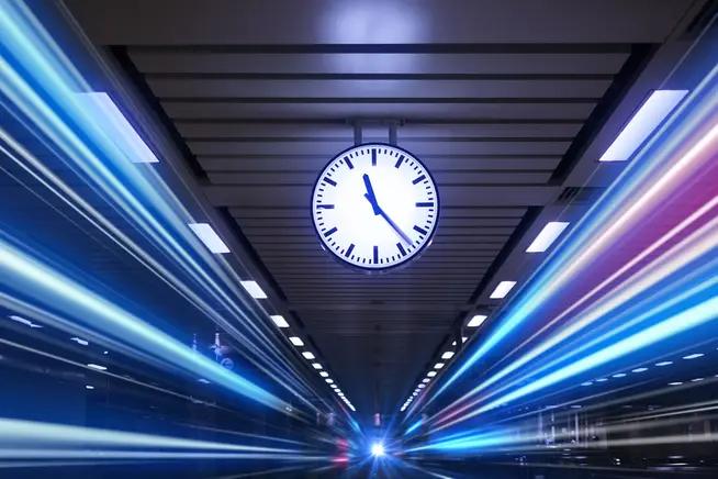 A clock mounted on a ceiling of a train station with vibrant light streaks suggesting movement.