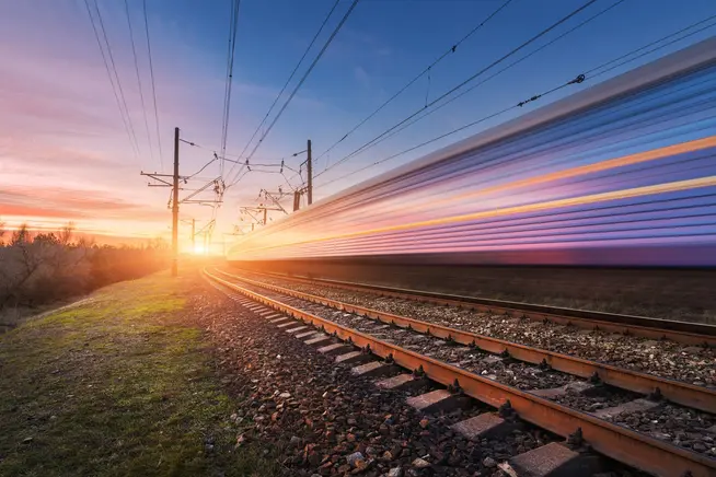 Schnellzug fährt bei Sonnenuntergang über Gleise, farbenfroher Himmel im Hintergrund.