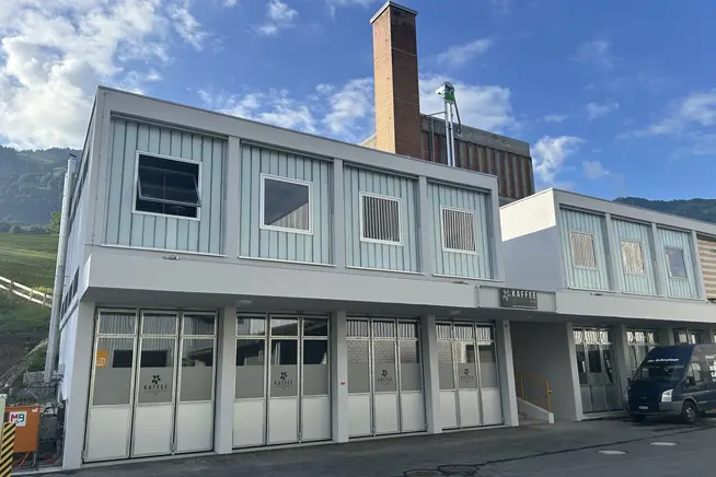 Moderne zweistöckige Gebäude mit großen Fenstern und Kamin, vor einem blauen Himmel.